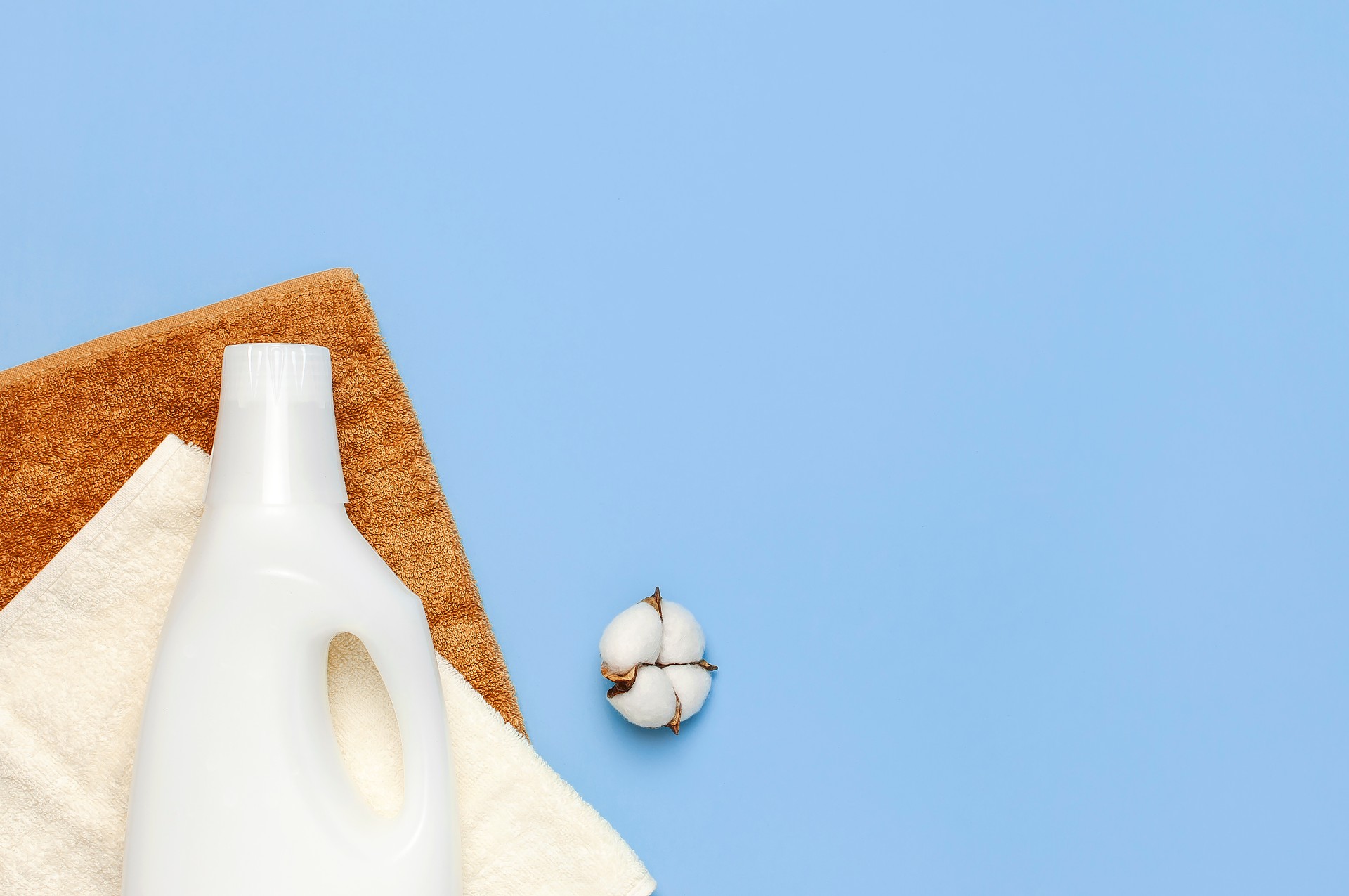 White plastic packaging of laundry detergent, liquid powder, washing conditioner, towels and cotton flowers on blue background. Flat lay top view copy space. Bio organic product. Eco cleaning concept